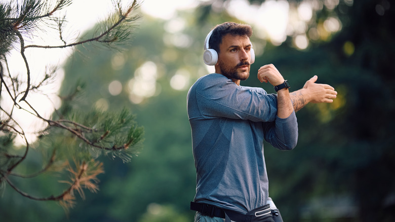 A person stretching before a workout in the woods while wearing over-the-ear headphones