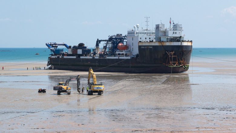 Lying on a beach out the water the cable laying ship Cable Enterprise supported by onshore workers is in the process of laying cables