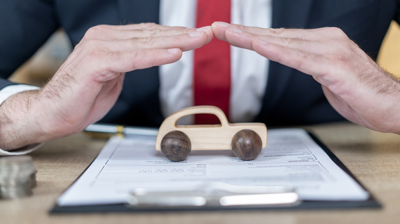 A person sitting in front of an insurance policy and a small wooden car.