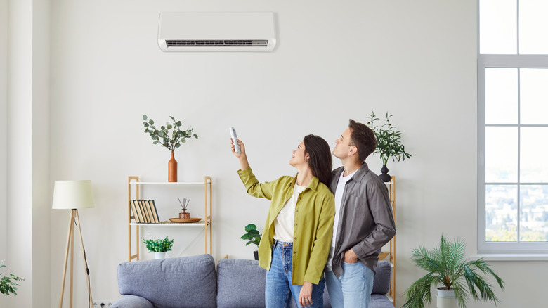 A couple turning on a wall-mounted air conditioner.