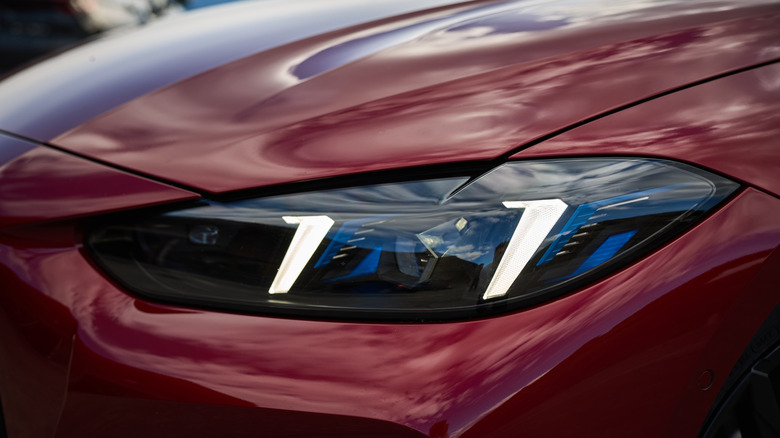 A close up of a front headlight of a red 2024 BMW M440i xDrive Coupé