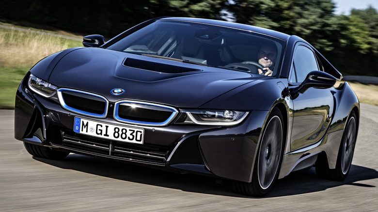Black BMW i8 driving on a sunny road with trees in the background