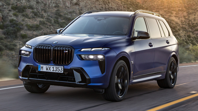 A blue BMW X7 SUV driving on an open highway with mountains in the background