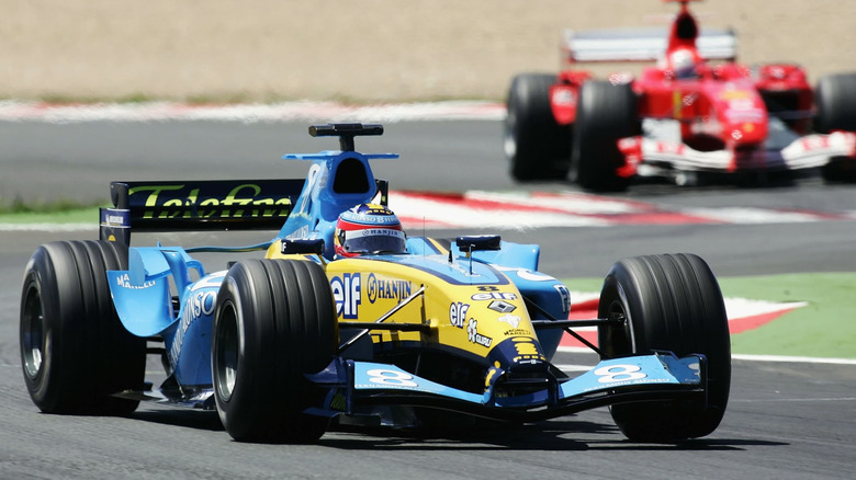 A yellow V-10-powered Renault R24 racing on a circuit, with a red F1 car trailing behind it.