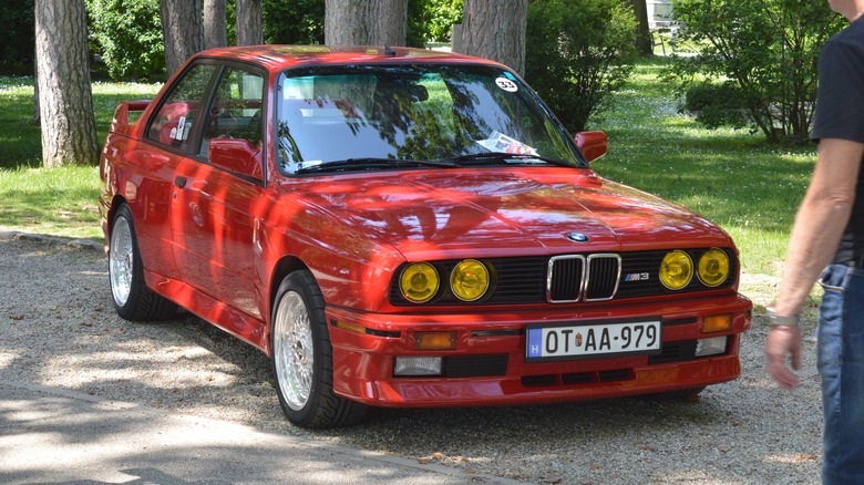 A red E30 BMW M3 with yellow headlights, front 3/4 view