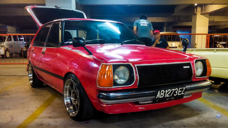 Front 3/4 view of red Mazda 323 in parking garage
