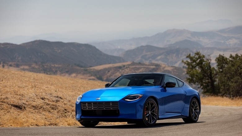 Blue 2023 Nissan Z parked by a roadside with trees and mountains in the background