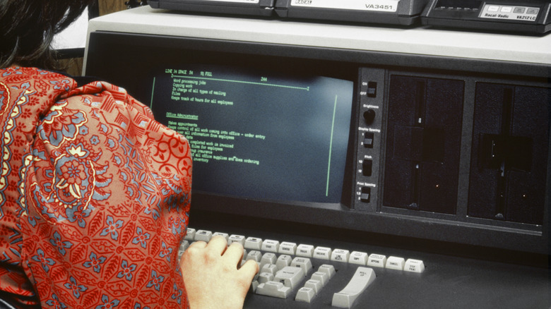 A woman in the 1980s working on a computer showing green text on a black background.