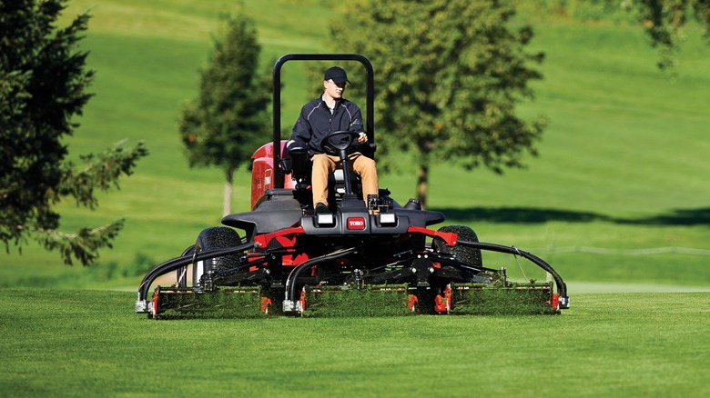 A grounds keeper using a commercial reel mower to maintain a golf course fairway