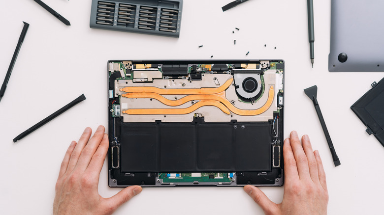 A MacBook with the back cover opened on a table with tools next to it