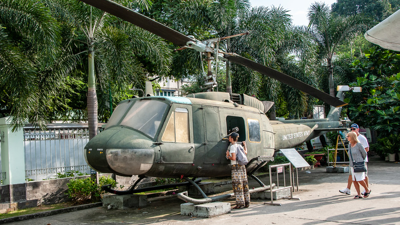 Personas que caminan mirando un viejo helicóptero Huey en bloques de cemento