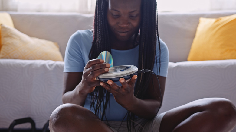 Someone loading a CD into a portable Sony CD player with an auxiliary cable plugged in.