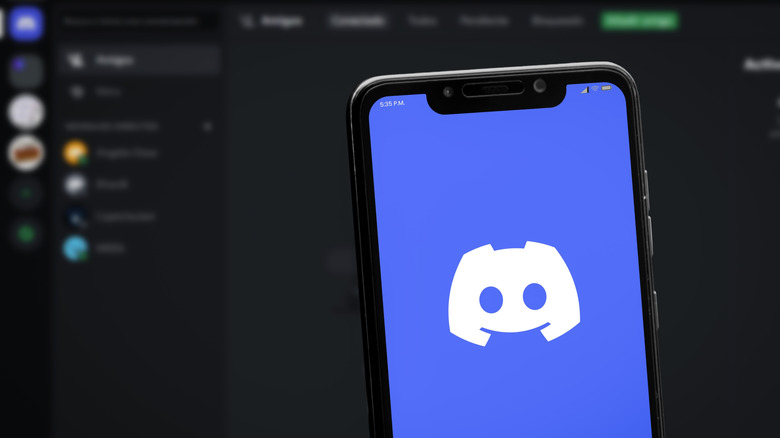 Discord app on a smartphone with a computer screen in the background.