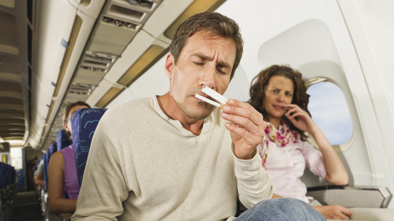 Smoker sitting in an airliner sniffing three unlit cigarettes