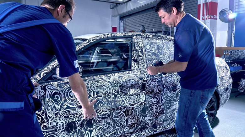 Technicians apply a stylized black-and-white camouflaging vinyl wrap to a Series 3 BMW prototype vehicle