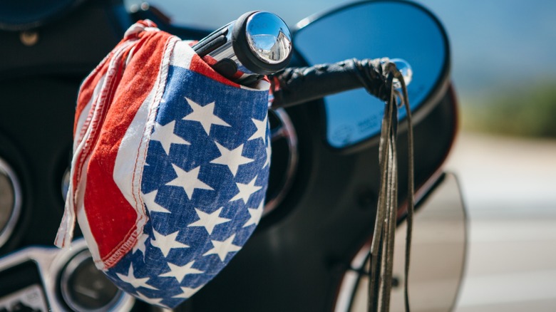 A stars and stripes bandana hanging on motorcycle handlebars.