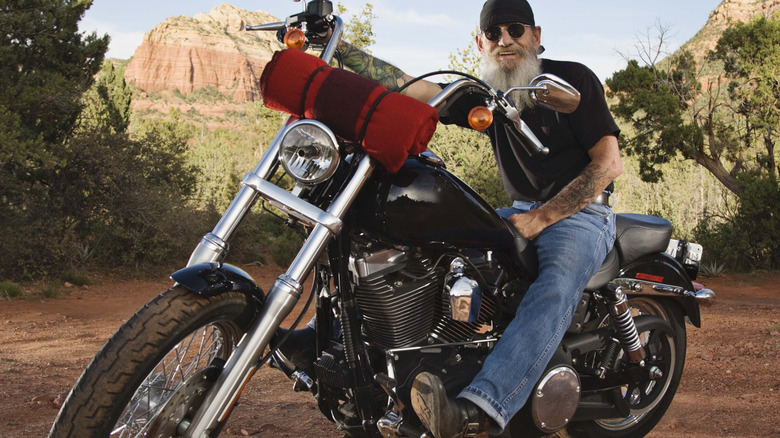 ﻿﻿A biker sits on a black motorcycle with a red blanket fastened to the front