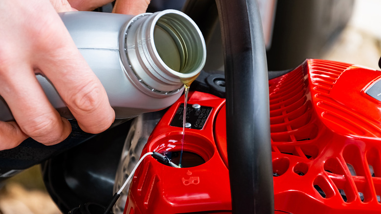 A person pouring oil into gasoline-powered chainsaw