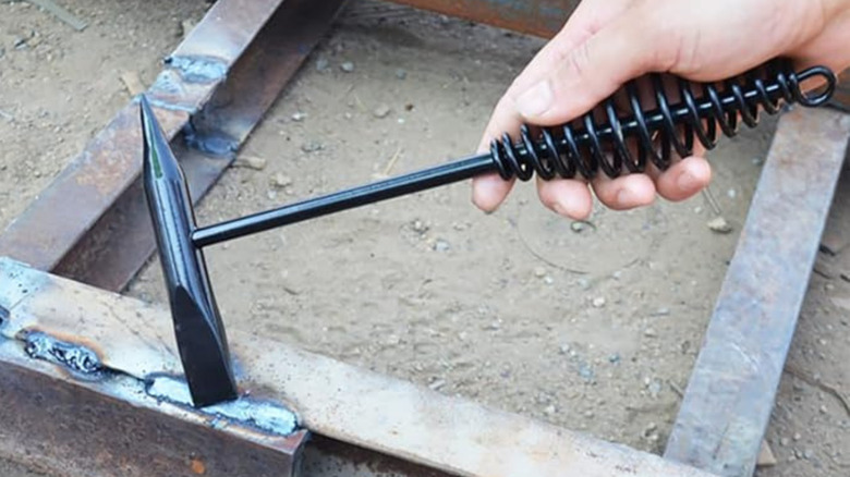 A person holding a chipping hammer with spring handle