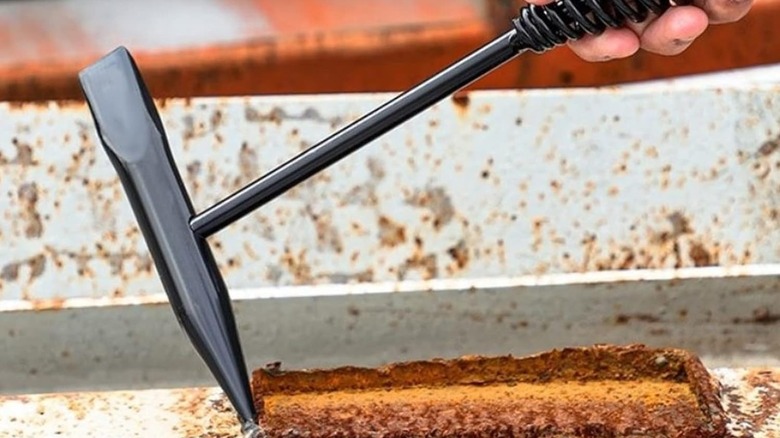 A person removing rust using a chipping hammer with spring handle