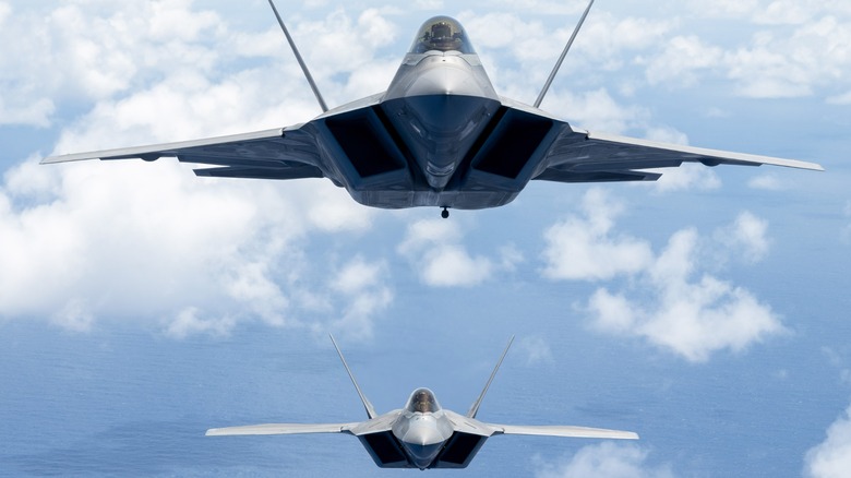 Two USAF F-22 Raptors flying together over lightly cloudy skies