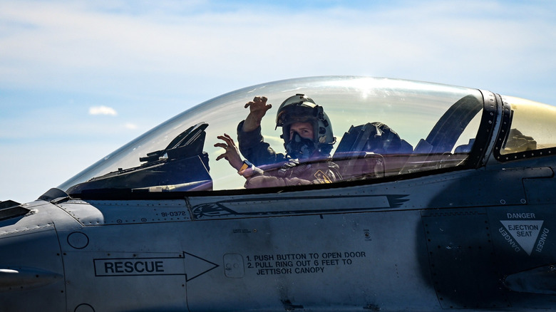 Fighter pilot performs claw motion with both hands.