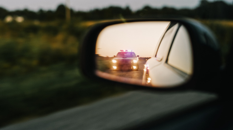 A vehicle side mirror showing a police car on the road behind it