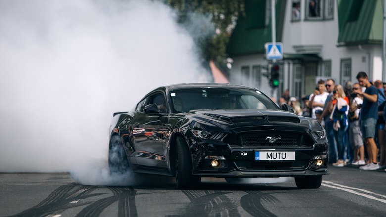 black Ford Mustang doing a burnout in front of a crowd