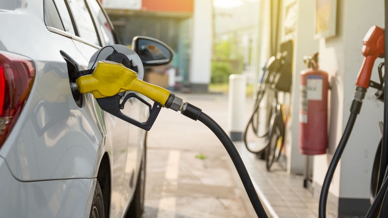 White car at gas pump with yellow nozzle inserted