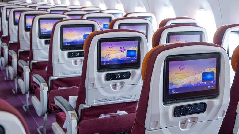 Inside of an empty passenger jet, showing the seat backs with all the inflight entertainment systems powered on