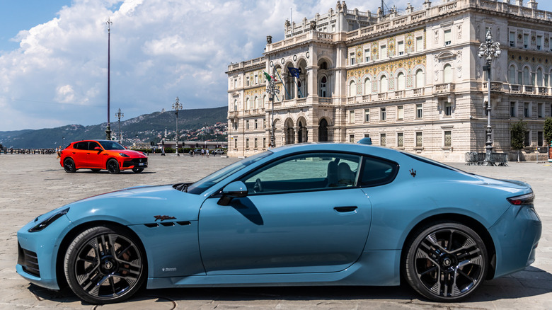 A blue Maserati GranTurismo and red Maserati Grecale in a plaza in Trieste, Italy