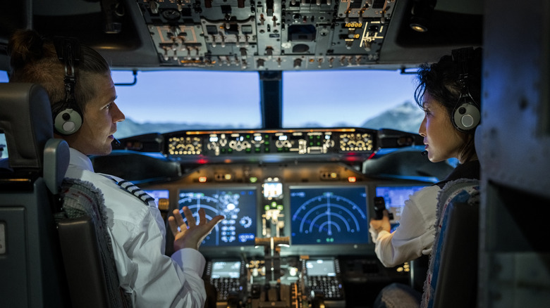 Rear view of a male pilot giving advice to female co-pilot while flying a modern jet airplane