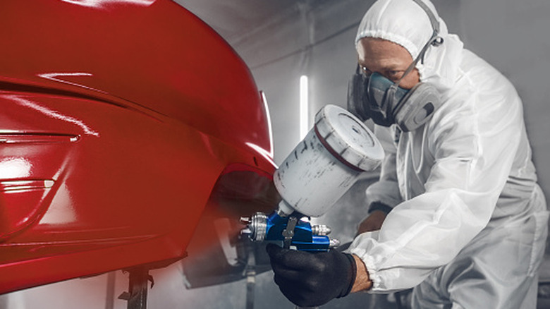 Professional car painter in chamber painting an automobile bumper red