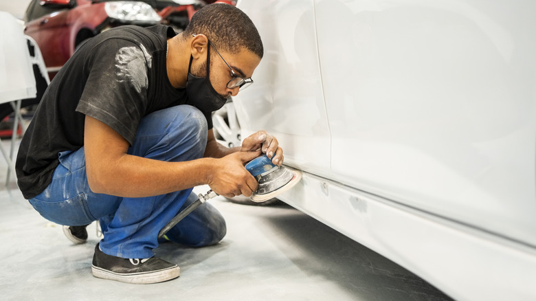 Auto mechanic wearing face mask using a grinding machine for sanding car rocker panel