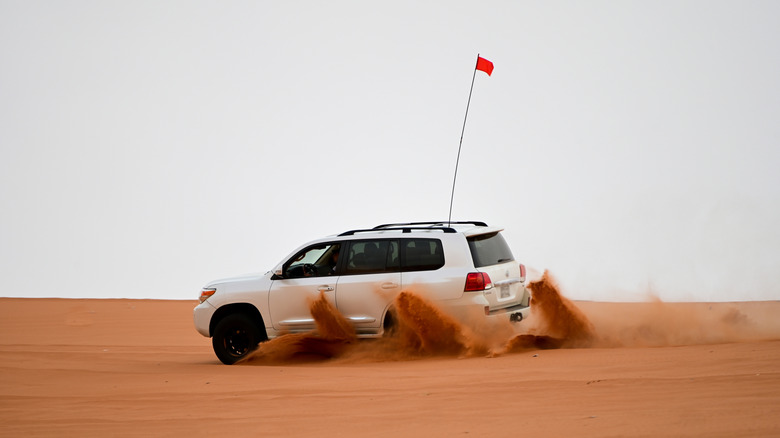 A white Toyota Land Cruiser driving on a sand dune with a flag mounted