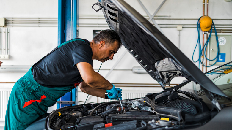 Professional car service mechanic worker standing in front of car engine open hood and working