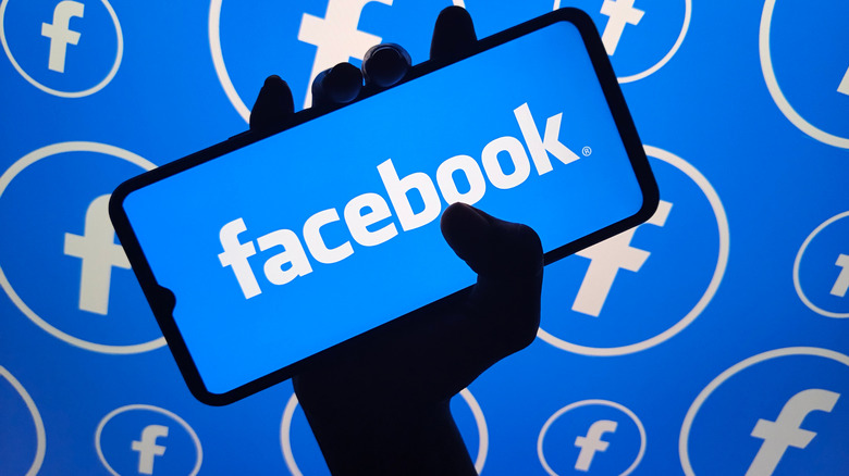 A silhouette of a hand holding a cellphone with the Facebook logo