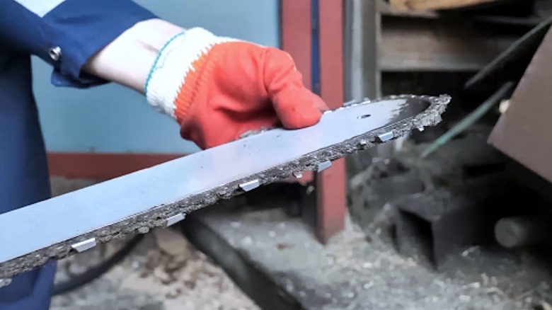 Gloved hand holding a chainsaw guidebar