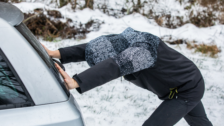 A man pushing a car in snowy rural outdoors.