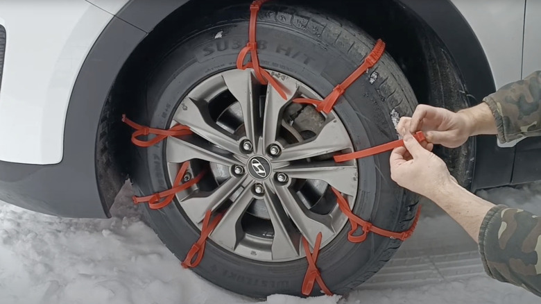 A person installing winter tire zip ties on a car on snow.