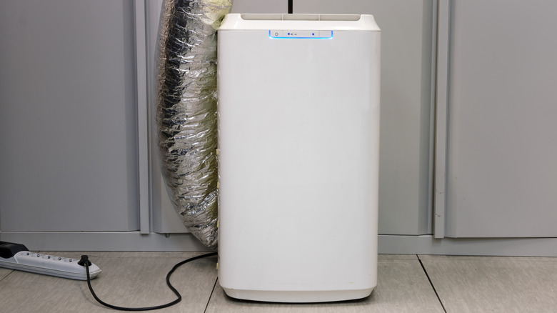 A portable air conditioner standing on a floor and plugged into a power strip.