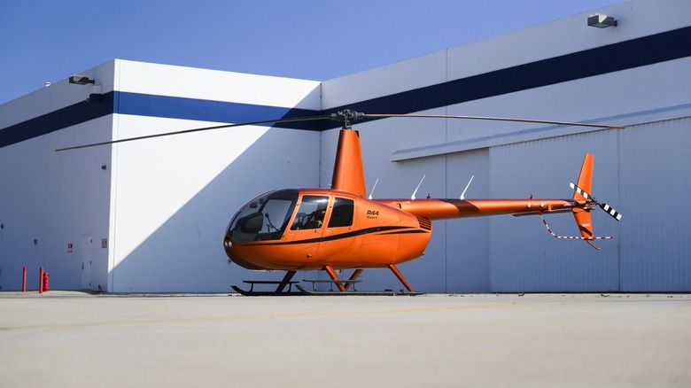 Robinson R44 helicopter in red parked outside a hanger.