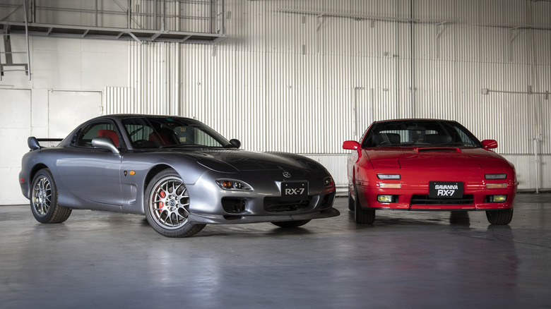 2002 Mazda RX-7 Spirit R and 1992 Mazda FC Savanna RX-7 side-by-side in hangar, front-right view on Spirit R, front-view on Savanna