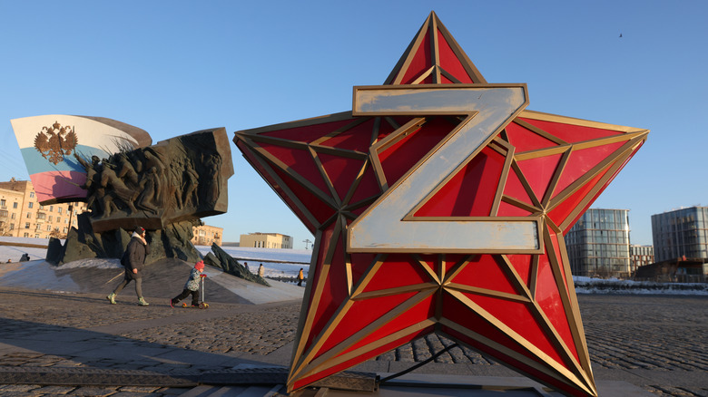 A mother and child walk through a Moscow square featuring a giant statue of the letter Z plastered on the front of a red star, symbolizing support for the invasion of Ukraine