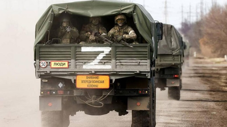 Armed Russian soldiers ride in the back of a military vehicle labeled with the infamous Z insignia