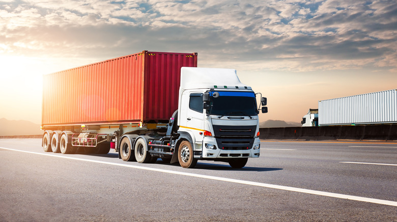 Semi-truck driving on the highway carrying a orange container