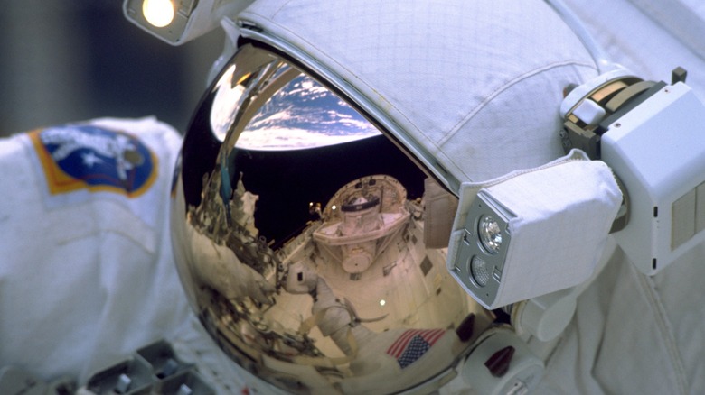 A NASA Astronaut's helmet reflecting the bay of the Space Shuttle Discovery and the Earth