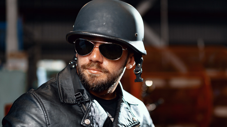 A bearded man motorcyclist in dark sunglasses on dark building background