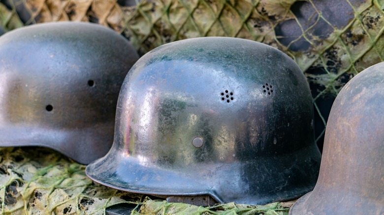 Close-up of a row of old German World War II military helmets arranged against a camouflage netting background