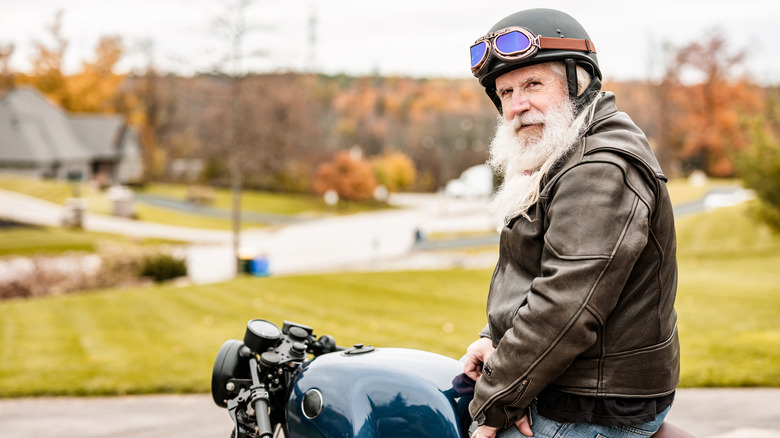 Senior man with grey long hair and beard getting ready to ride his motorcycle